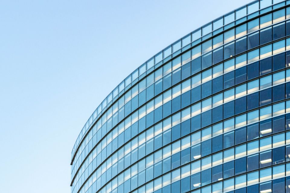 Gerundete Glasfassade eines Bürogebäudes vor hellem Himmel.
