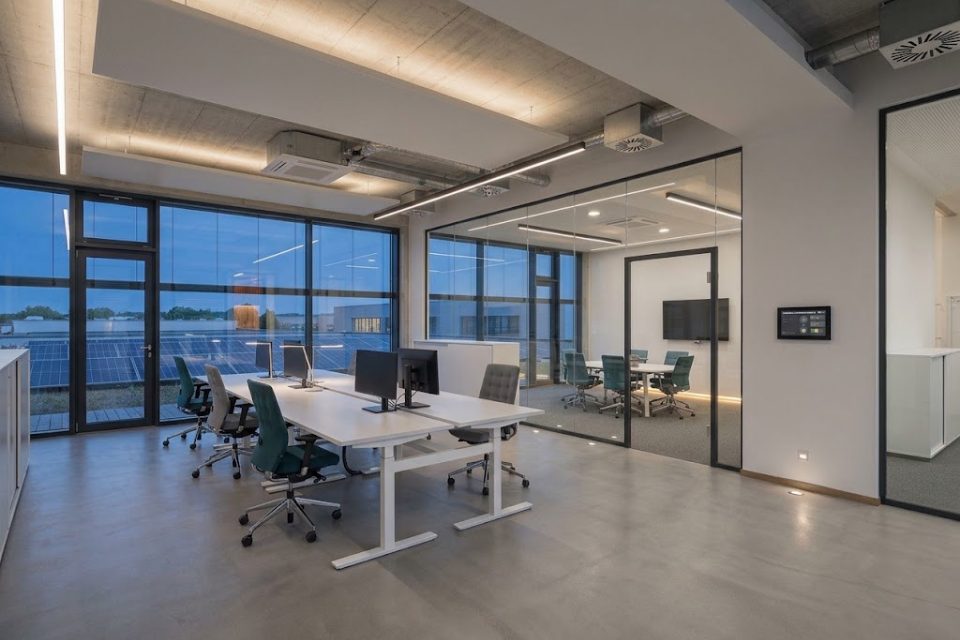 Büro mit Heiz- und Kühlsegeln unter der Betondecke, Lüftungsauslässen, Wandpanel und Photovoltaik vor dem Fenster.